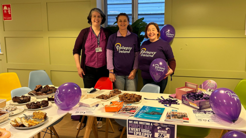 Three women in Epilepsy Ireland t-shirts hosting a Purple Day event.