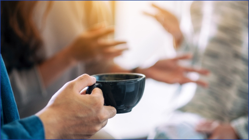 Person holding a blue cup with people talking in the background