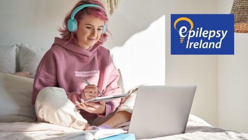 Teenager on Laptop taking notes and smiling with Epilepsy Ireland logo in top RHS corner