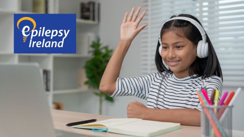 Child raising hand while on laptop with Epilepsy Ireland logo in LHS corner