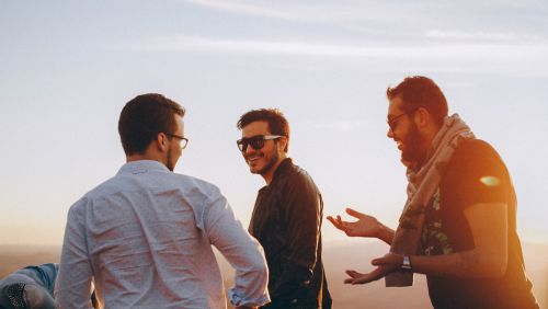 Three men walking on a beach talking to each other and laughing 