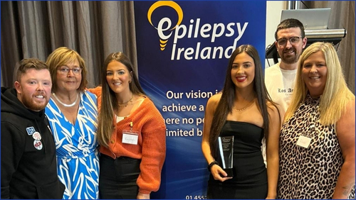 Thomas, Bernie, Kayleigh, Mileaha, Graham and Rhona pictured in front of an Epilepsy Ireland sign posing with their Volunteer of the Year award